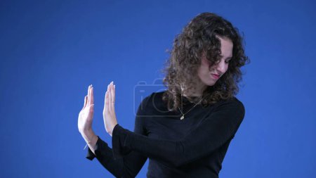Foto de 20s Mujer expresando rechazo y disgusto con gesto de mano, mujer empujando con las manos hacia los lados sobre fondo azul - Imagen libre de derechos