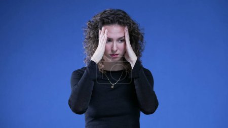 Photo for Desperate woman struggling with regret and bad memories from past standing on blue background covering face with hands feeling mental pain - Royalty Free Image