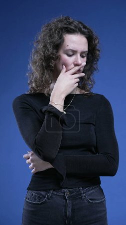 Foto de Mujer pensativa pensando profundamente en la decisión con la mano en la barbilla en el fondo azul. Caucásico persona femenina en 20s emoción pensativa, ponderando dilema - Imagen libre de derechos