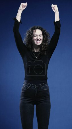 Photo for Woman Exulting in Success with Upward Fist, Blue Background in Vertical Orientation - Royalty Free Image
