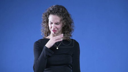 Photo for Woman showing revulsion to bad odor waving hand in disgust while standing on blue background and looking at camera - Royalty Free Image