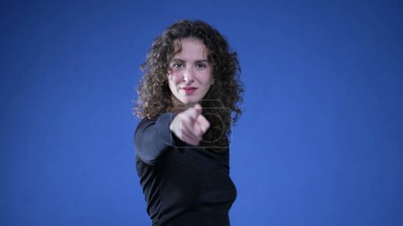 Photo for Woman pointing finger at camera signalling "YOU" with hand gesture standing on blue background - Royalty Free Image