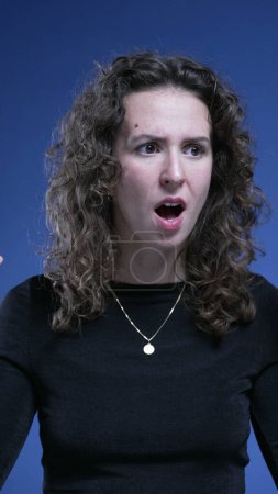 Foto de Mujer joven asustada reaccionando con SHOCK y sorpresa ante noticias inesperadas sobre fondo azul capturado - Imagen libre de derechos