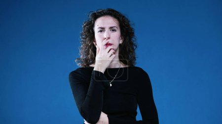 Photo for Woman contemplative decision making while squinting and with hand in chin pondering solution gazing at distance on blue background - Royalty Free Image