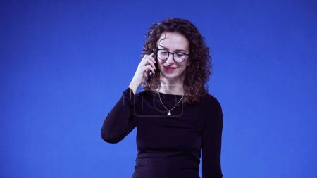 Téléchargez les photos : Femme parlant au téléphone debout sur fond bleu. Une femme de 20 s parlant avec un appareil de téléphone portable - en image libre de droit
