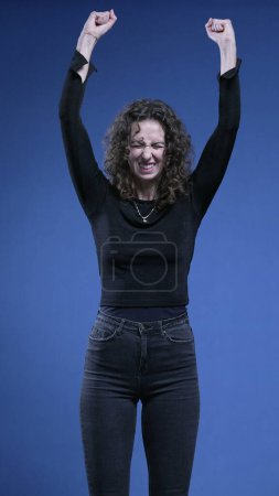 Foto de Mujer victoriosa levanta puño y brazos en el aire celebrando el logro, telón de fondo azul - Imagen libre de derechos