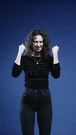 Téléchargez les photos : Femme exultant dans le succès avec le poing vers le haut, fond bleu dans l'orientation verticale - en image libre de droit