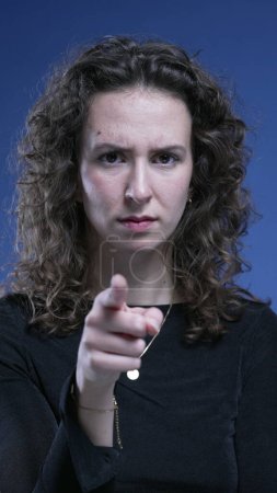 Femme bouleversée accusant spectateur en pointant du doigt vers la caméra sur fond bleu