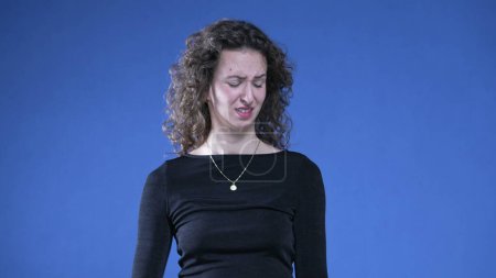Photo for Woman showing revulsion to bad odor waving hand in disgust while standing on blue background and looking at camera - Royalty Free Image