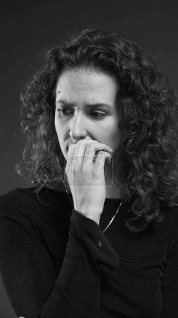 Photo for Despairing woman struggling with crippling anxiety by biting nails and ruminating past events in dramatic monochromatic, black and white - Royalty Free Image
