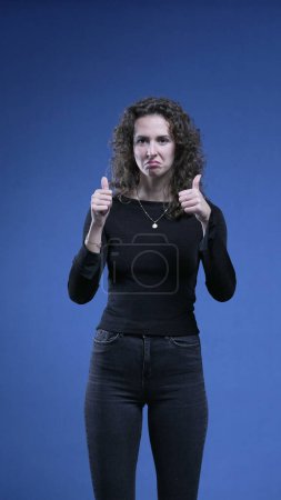 Photo for Woman showing signs of approval by giving THUMBS UP and giving OK sign with hand, applauds to camera engaging and supporting cause looking directly at camera - Royalty Free Image