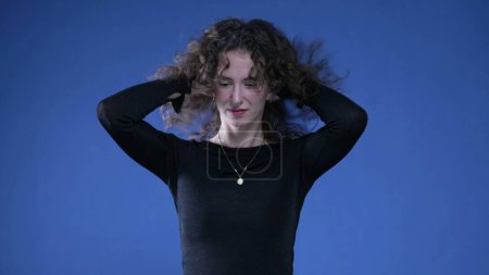 Photo for Woman playing with her hair shaking while standing on blue background - Royalty Free Image