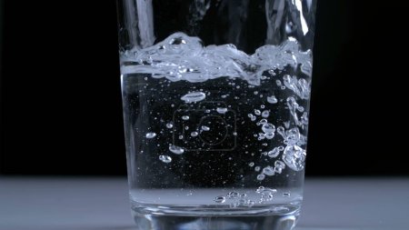 Téléchargez les photos : L'eau étant versée dans une tasse transparente en verre au ralenti super à 1000 ips en fond noir - en image libre de droit