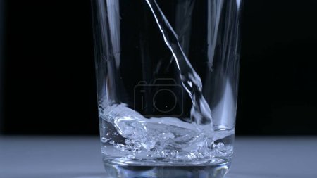 Téléchargez les photos : Verser de l'eau dans une tasse en verre au ralenti capturé avec une caméra haute vitesse en toile de fond noire - en image libre de droit