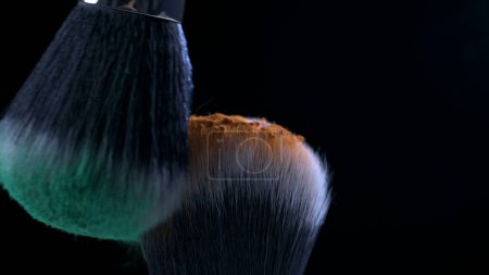 Photo for Macro close-up of cosmetic brushes clashing in super slow motion captured with a high speed camera at 1000 fps with orange and green powder flying in the air - Royalty Free Image