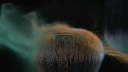 Foto de Macro primer plano del cepillo cosmético capturado con una cámara de alta velocidad a 1000 fps con polvo naranja y verde volando en el aire - Imagen libre de derechos
