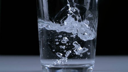 Foto de Agua que se vierte en una taza transparente de vidrio en cámara súper lenta a 1000 fps en fondo negro - Imagen libre de derechos