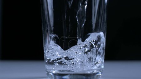 Photo for Pouring water into glass cup in super slow-motion captured with high-speed camera in black backdrop - Royalty Free Image