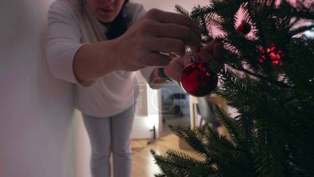 Téléchargez les photos : Préparation pour les vacances d'hiver - Femme Ajout d'ornement de boule de Noël à l'arbre - en image libre de droit