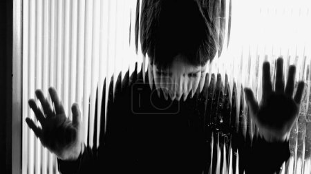 Foto de Niño atrapado en la lucha mental, apoyado en la ventana en la desesperación, capturado en monocromo, dramático blanco y negro - Imagen libre de derechos
