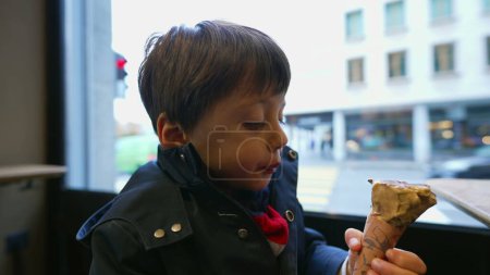 Photo for Boy Savoring Ice Cream cone at Parlor with City View in background - Royalty Free Image