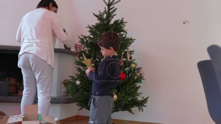 Téléchargez les photos : Mère et enfant Décorer l'arbre de Noël avec des boules et des ornements - Adopter les traditions des fêtes. Jeune garçon voulant mettre Star sur le dessus - en image libre de droit