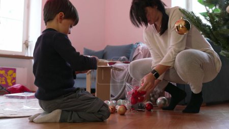 Téléchargez les photos : Mère et enfant se préparent pour les fêtes de Noël, ornements de boule de déballage dans le plancher du salon à côté de l'arbre - en image libre de droit