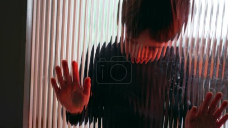 Foto de Niño aburrido solitario apoyado en una ventana de vidrio con problemas de color rojo teñido con nada que ver - Imagen libre de derechos