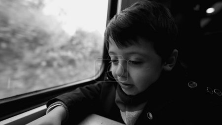 Téléchargez les photos : L'enfant voyage en train assis par la fenêtre avec un paysage qui passe, capturé en monochrome, noir et blanc - en image libre de droit