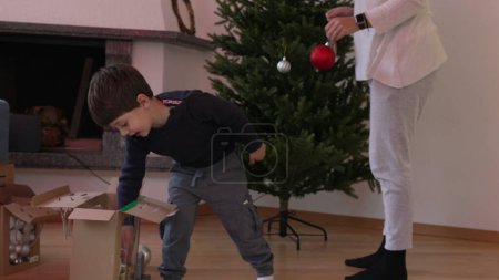 Téléchargez les photos : Mère et enfant plantant l'arbre de Noël par des ornements de boule de déballage pour la décoration, famille franche préparant des festivités de vacances - en image libre de droit