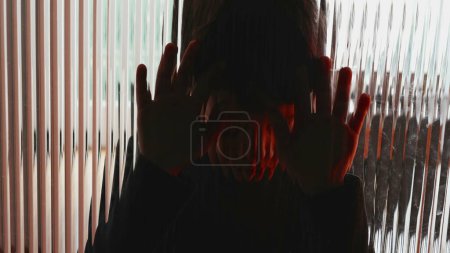 Foto de Deprimido niño apoyado en la ventana de cristal sensación de tristeza y desesperación luchando con enfermedades mentales en la infancia - Imagen libre de derechos