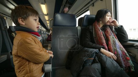 Téléchargez les photos : Mère et enfant voyageant en train ensemble, petit garçon debout sur le couloir tandis que maman regarde la vue en passant par l'intérieur du transport à grande vitesse européen - en image libre de droit