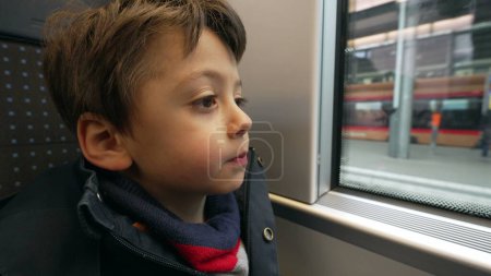 Téléchargez les photos : Jeune garçon casse-croûte tout en voyageant en train regardant quai de transport à grande vitesse européenne. Pensive enfant manger des biscuits pendant le trajet - en image libre de droit