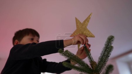 Téléchargez les photos : Enfant mettant une étoile sur le sapin de Noël, célébrant la tradition. Petit garçon plaçant l'ornementation pendant les festivités de la saison d'hiver - en image libre de droit