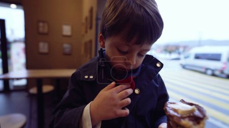 Photo for Child accidentally stains scarf with ice-cream cone while eating treat at parlor, wearing jacket. Mother adjusts son's clothes to protect from smudge - Royalty Free Image