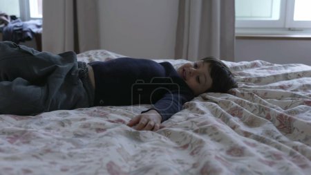 Photo for Energetic Child bouncing in bed, carefree emotion of little boy having fun by himself in paren't beedroom jumping up and down in bedsheets - Royalty Free Image