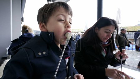 Photo for Mother and child enjoying Swiss fondue at restaurant while traveling on vacation. Close-up of kid blowing on bread with cheese - Royalty Free Image