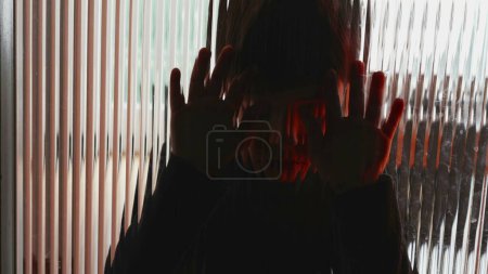 Photo for Depressed child leaning on glass window feeling sadness and despair struggling with mental illness in childhood - Royalty Free Image