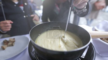 Téléchargez les photos : Nourriture suisse traditionnelle, fourchette à gros plans avec trempette de pain dans le fromage, peopel dégustant de la nourriture d'hiver par temps froid - en image libre de droit