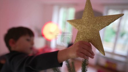 Foto de Niño colocando la estrella en el árbol de Navidad con la ayuda de la madre - Momento de fiesta familiar - Imagen libre de derechos