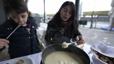 Photo for Closeup of traditional Swiss fondue, people eating bread with cheese at outdoor restaurant enjoying European food during winter season - Royalty Free Image