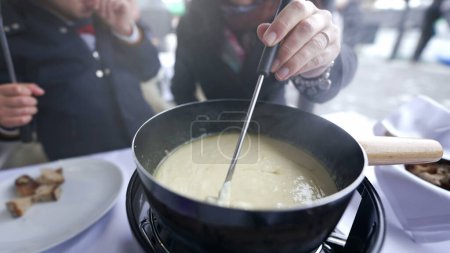 Photo for Traditional Swiss food, closeup hand holding fork with bread dipping in cheese, peopel enjoying winter food in cold weather - Royalty Free Image