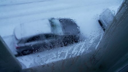Téléchargez les photos : Vue de la fenêtre de l'appartement regardant dehors pendant la journée enneigée, POV de la personne regardant dehors avec la rue et les voitures garées couvertes de neige, vers la maison - en image libre de droit