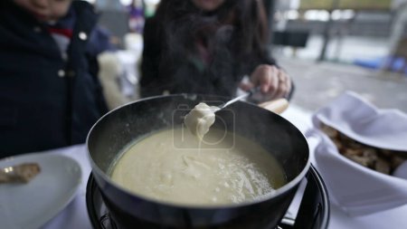 Téléchargez les photos : Gros plan de fondue suisse traditionnelle, les gens qui mangent du pain au fromage au restaurant en plein air dégustant de la nourriture européenne pendant la saison d'hiver - en image libre de droit