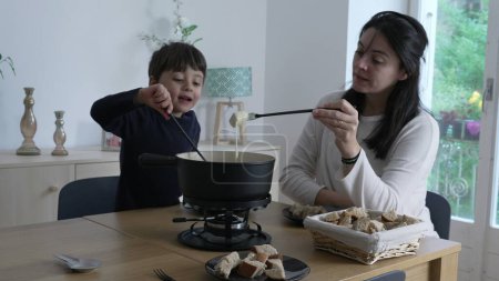 Photo for Fondue at home, Mother and child eating traditional Swiss food, bread and cheese. Mom and son bonding over food at lunch time - Royalty Free Image