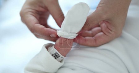 Photo for Mother putting small glove into newborn baby infant - Royalty Free Image