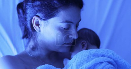 Foto de Mother holding newborn baby at hospital next to violet phototherapy lamp, real life affection and love - Imagen libre de derechos