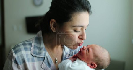 Foto de Mother holding newborn baby kissing infant, showing love after birth - Imagen libre de derechos