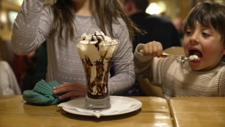 Foto de Hermano pequeño y hermana disfrutando de helado con crema batida - Salida de fin de semana familiar en el restaurante Diner - Imagen libre de derechos