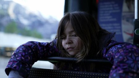 Foto de Pensive little girl becoming sad while leaning on bus seat by window. Closeup face of melancholic child lost in thought and introspection - Imagen libre de derechos